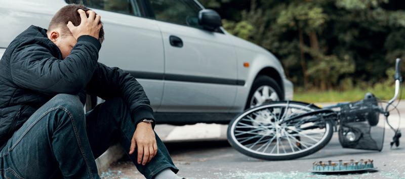 Man sitting next to his car and his bike, grabbing his head.