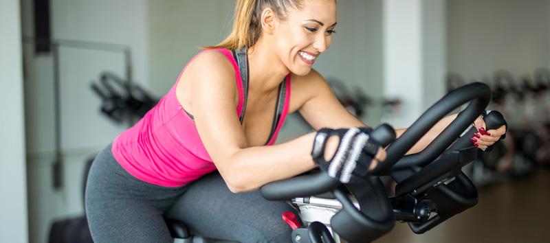 A young woman is smiling while riding a stationary bike.