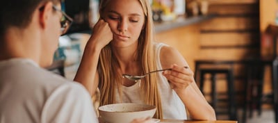  Una mujer joven está sentada en una mesa mirando fijamente su cuchara.