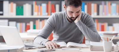 Un giovane uomo seduto in una biblioteca che legge un libro al tavolo.